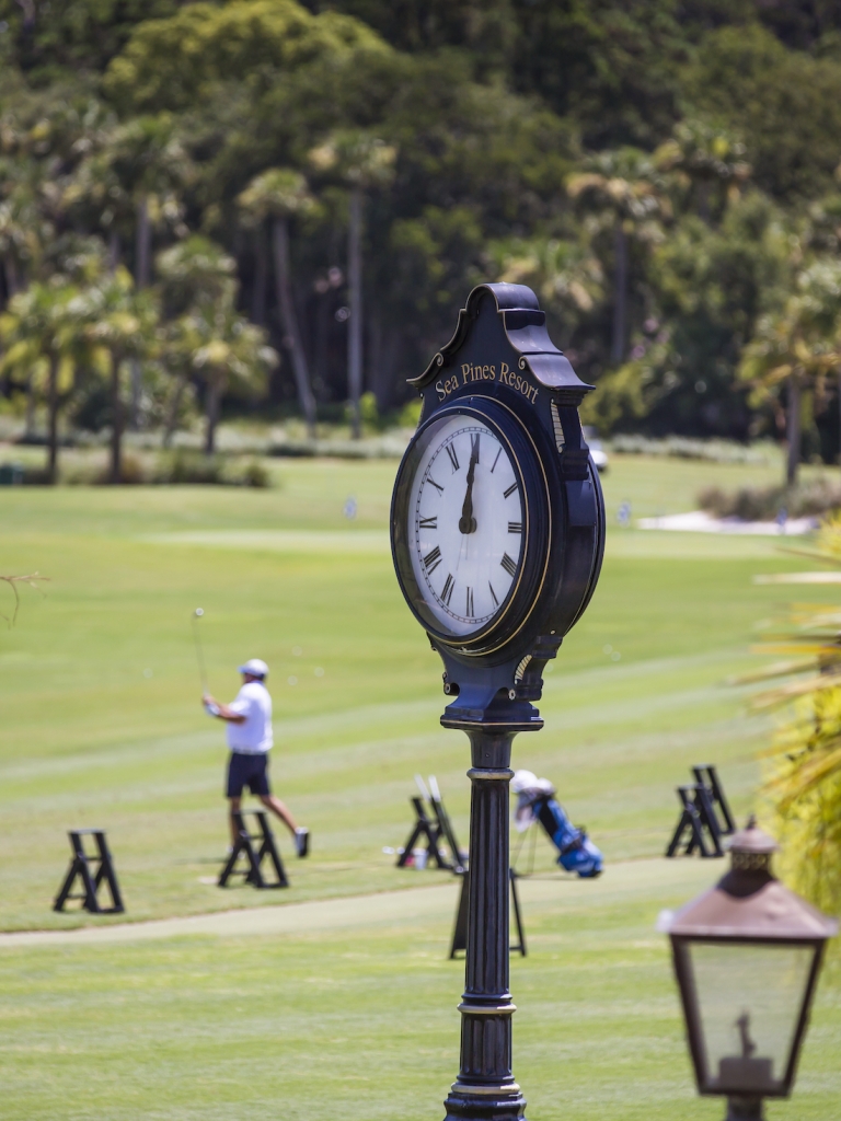 Image focused on a clock with the driving range in the background 