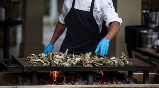 Chef moving oysters around on flat top grill at Oyster Roast event at Coast, Oceanfront Dining. 