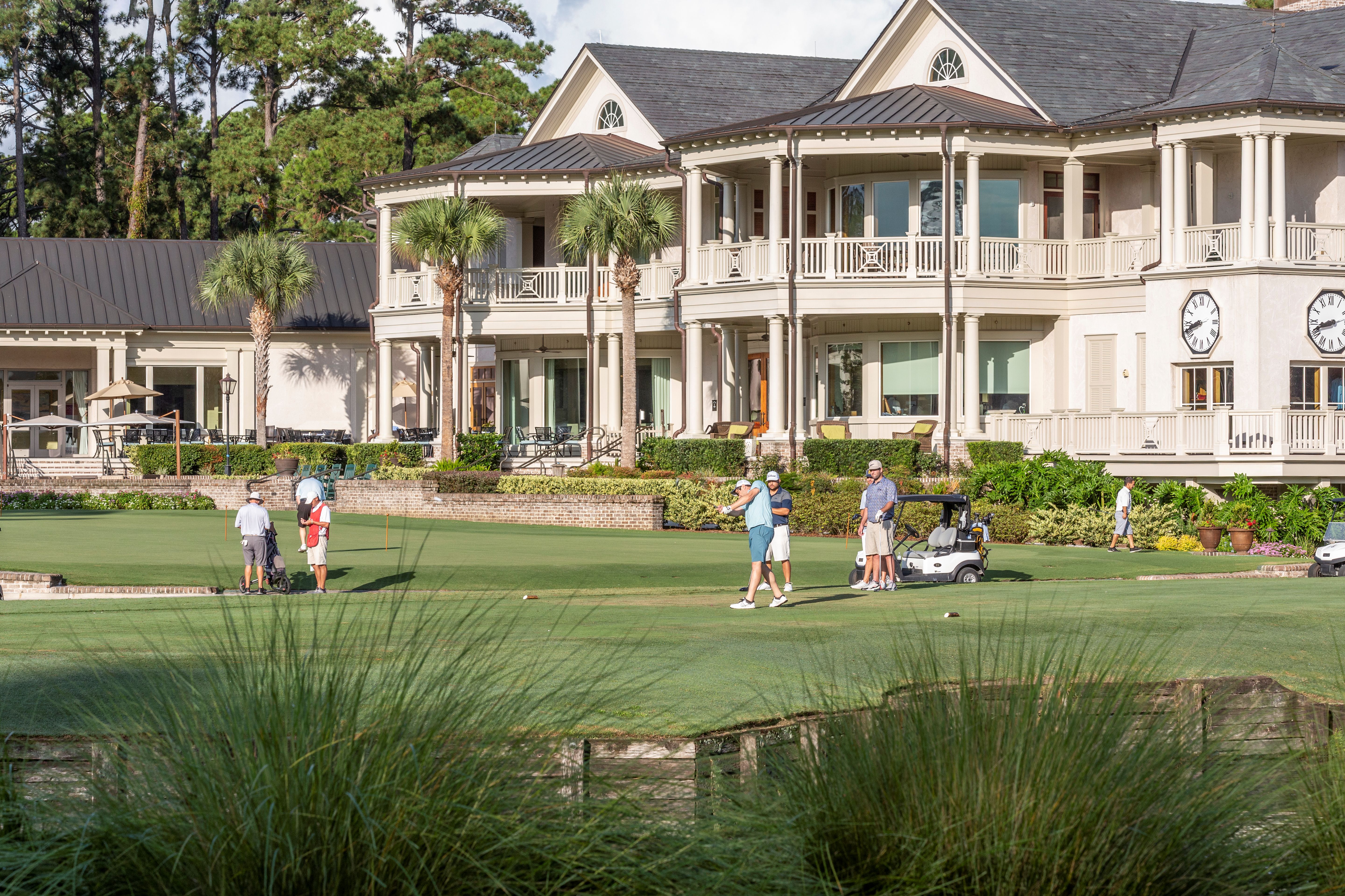Golfers play on a green at Harbour Town Golf Links in front of The Inn & Club at Harbour Town at The Sea Pines Resort. The clubhouse-style hotel features wraparound porches, palm trees, and views of the manicured golf course on Hilton Head Island.