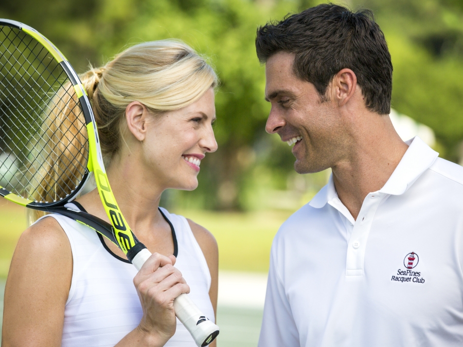 A women with a tennis racked talk to a man 