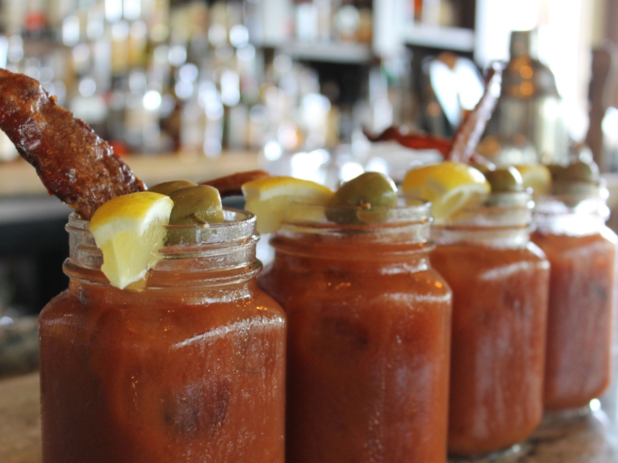 Bloody Mary's lined up along the bar with olive and bacon toppings. 