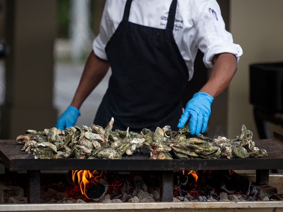 Chef moving oysters around on flat top grill at Oyster Roast event at Coast, Oceanfront Dining. 