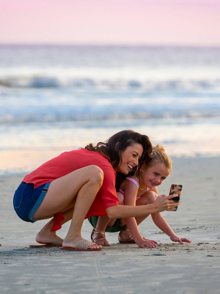 Mom and daughter taking a selfie with the beach in the background 