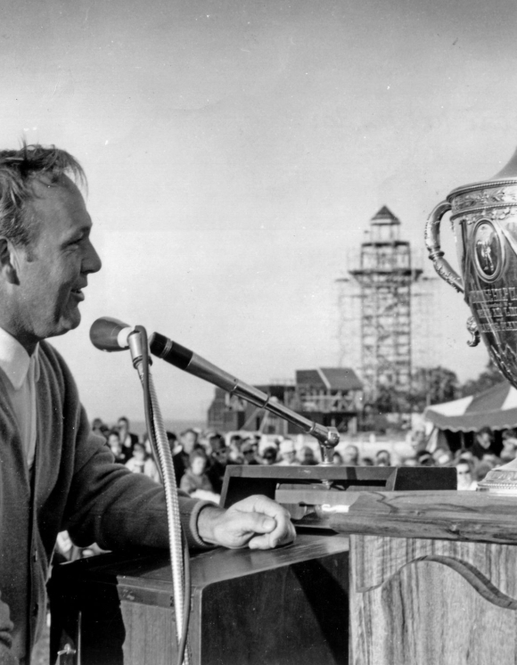 Man speaking into a microphone with a trophy beside him 