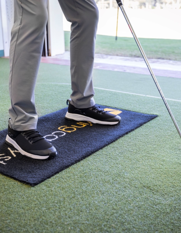 A golfer with a club and ball standing on the Swing Catalyst pad. 