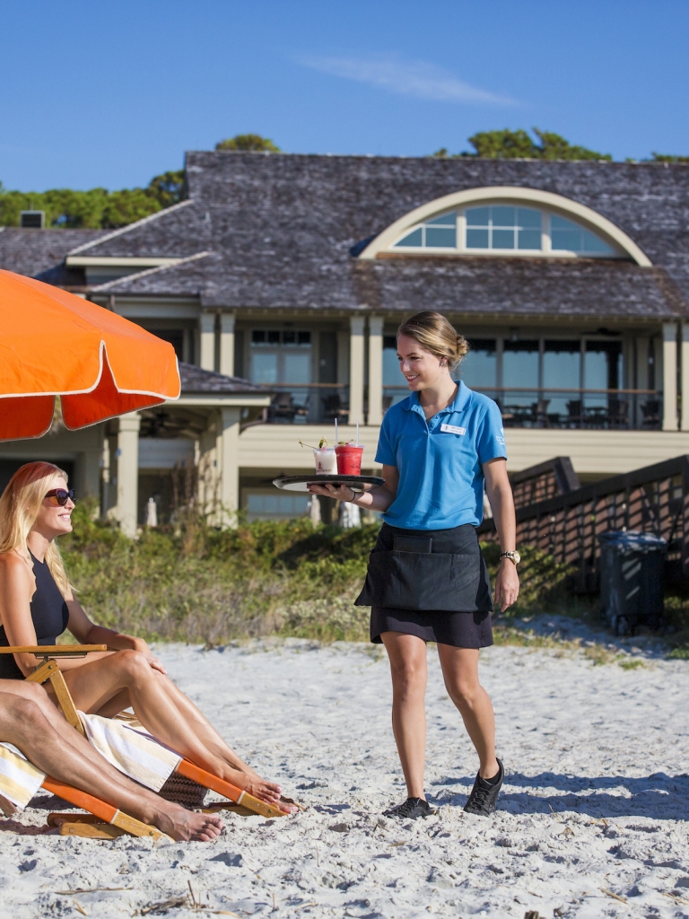 Waitress bringing drinks to a couple lounging on a beach 
