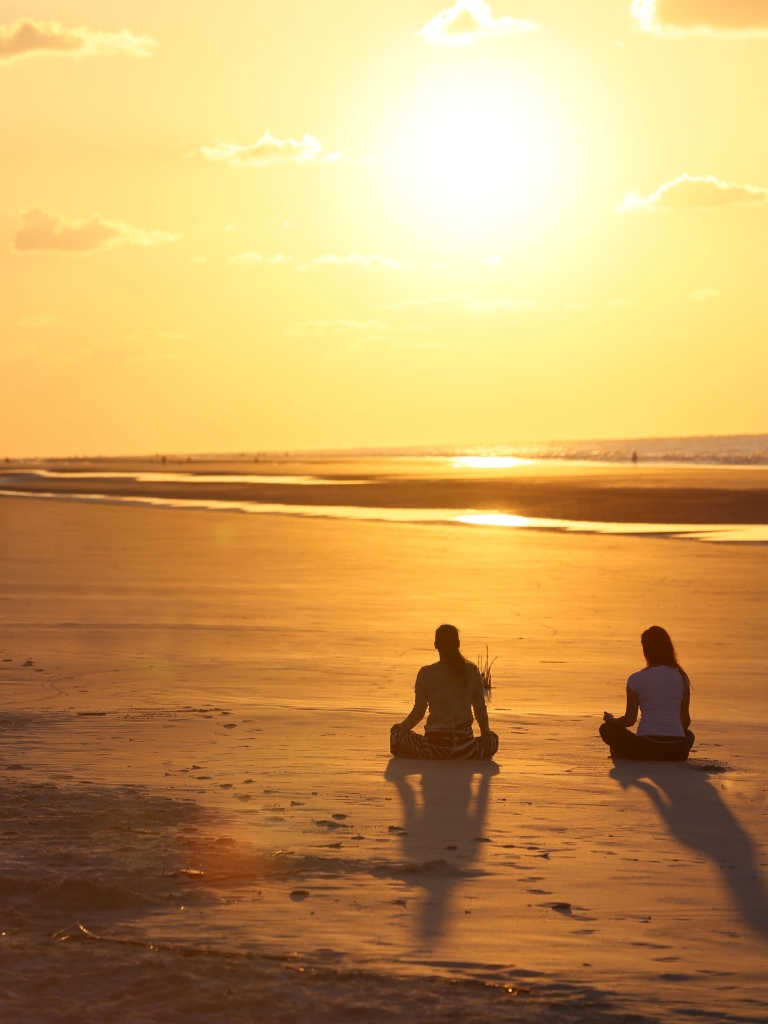 Two people doing yoga on the beach 