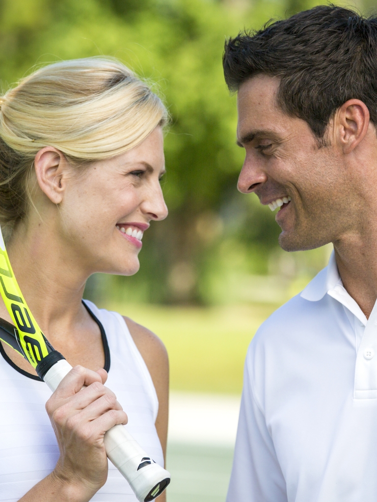 A women with a tennis racked talk to a man 