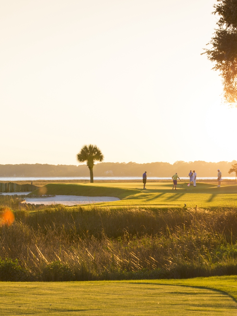 A group of golfers on the course at sunset 