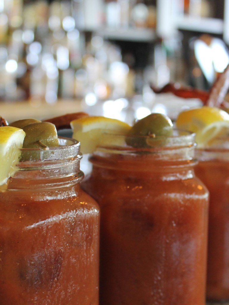 Bloody Mary's lined up along the bar with olive and bacon toppings. 