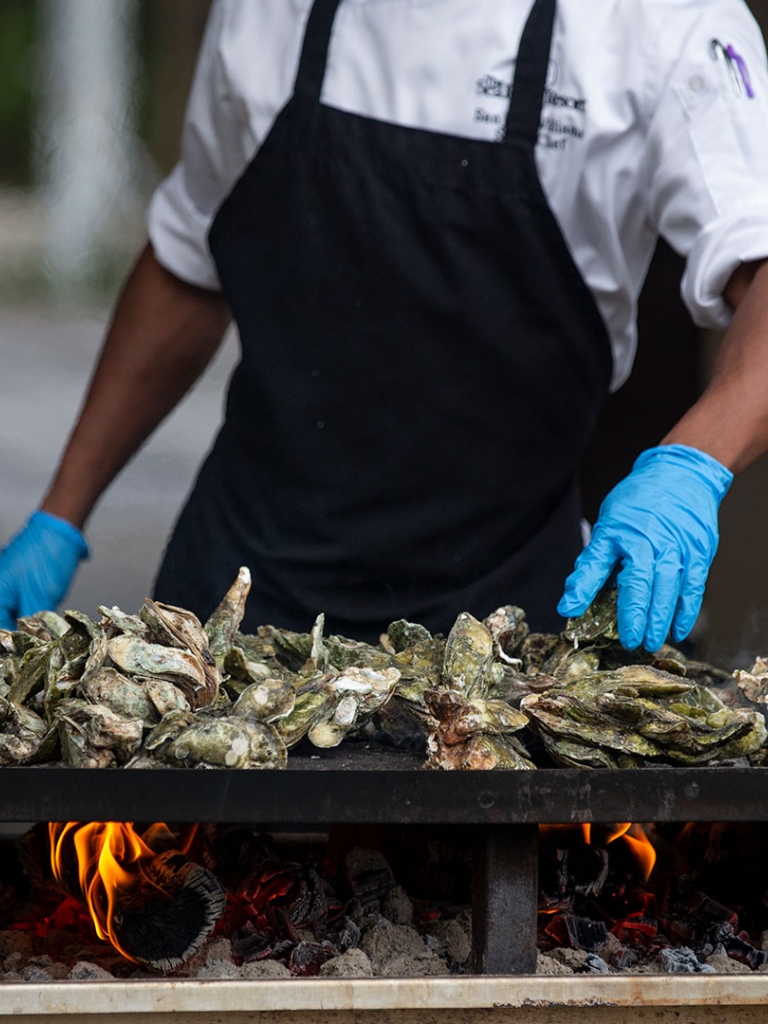 Chef moving oysters around on flat top grill at Oyster Roast event at Coast, Oceanfront Dining. 