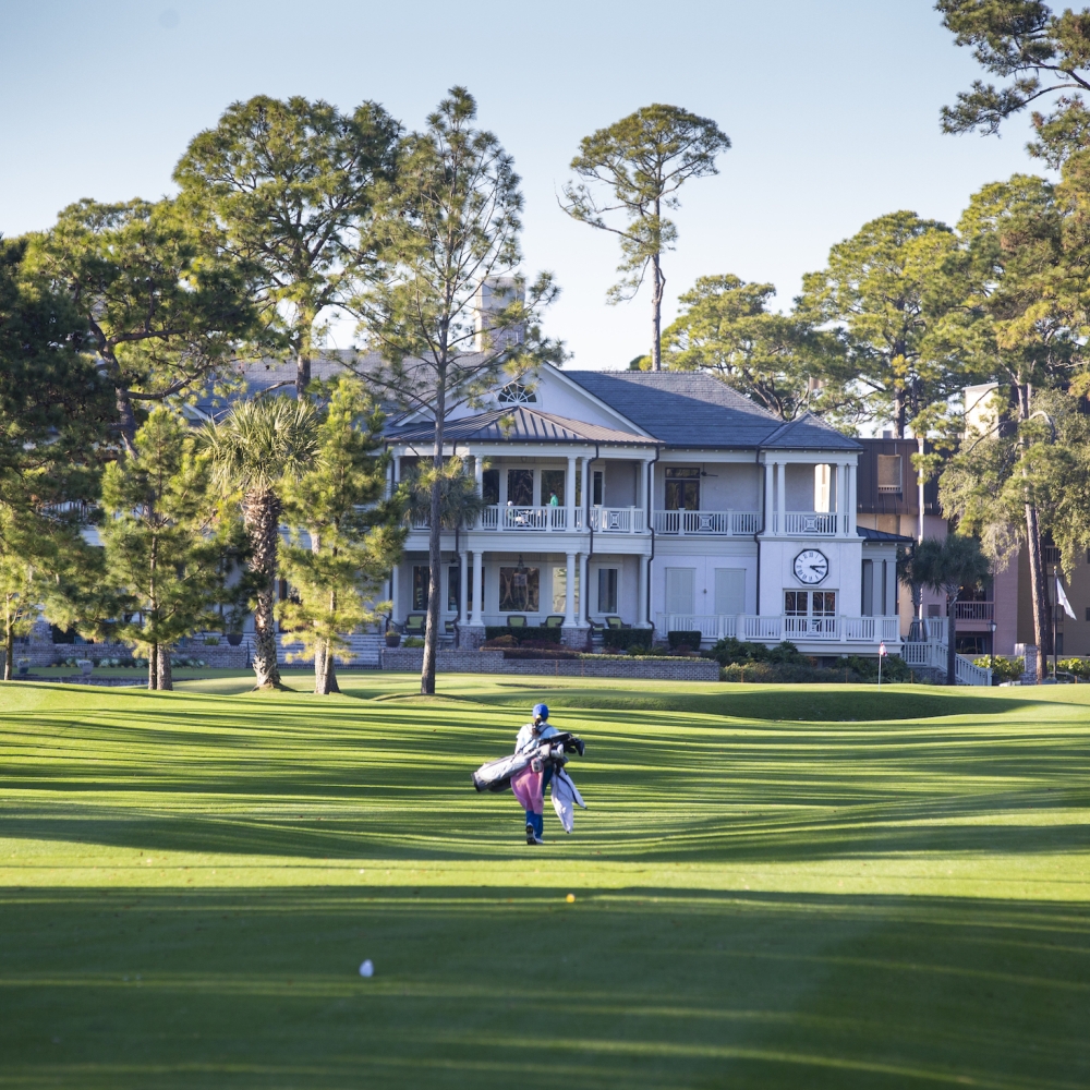 One golfer walking the course with the inn in the background  